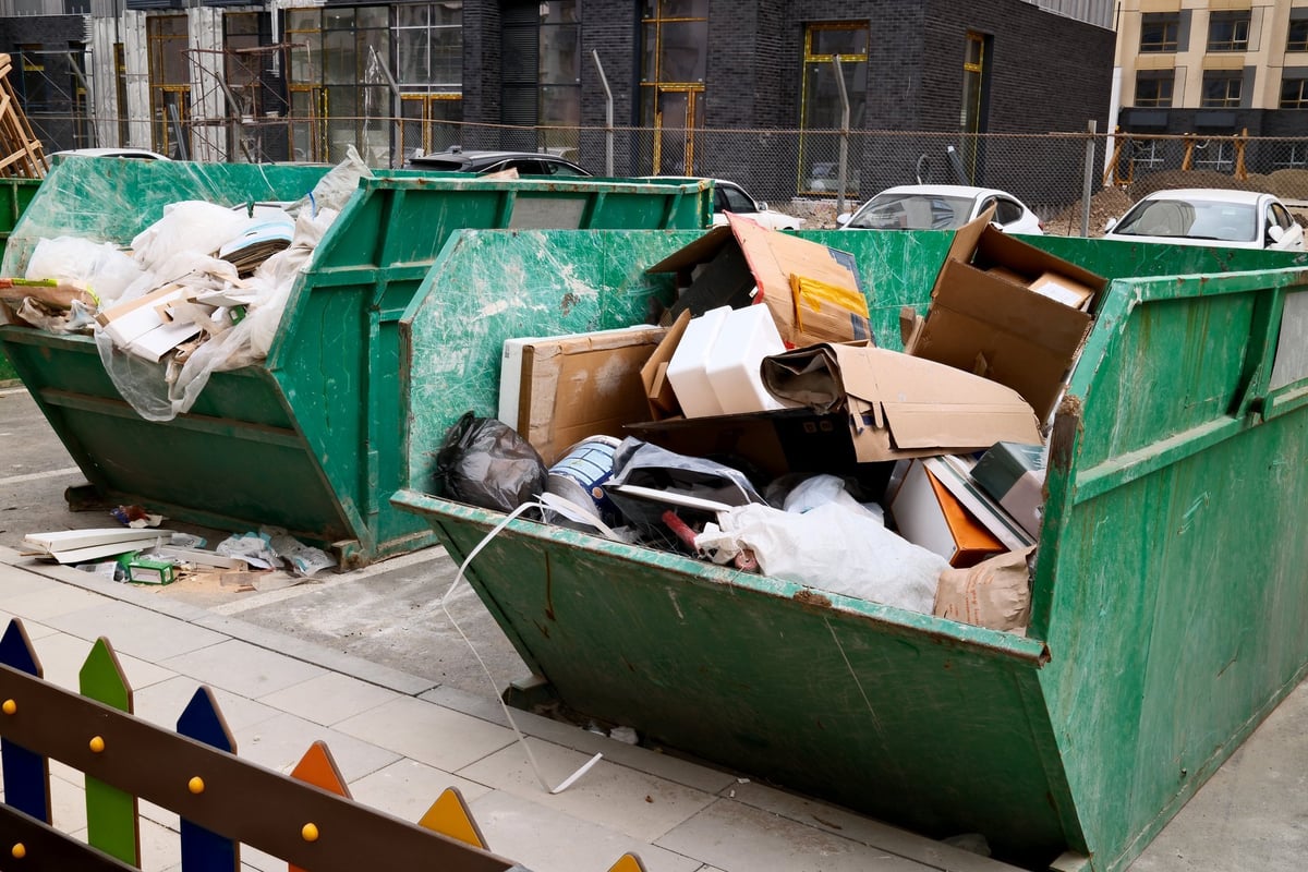 Overflowing green construction dumpster filled with cardboard boxes and building waste at urban construction site